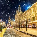 Декабрь город в огнях: новогодняя ёлка, украшенные здания и падающий снег на вечерней улице.